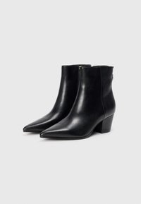Bottines en cuir noir avec un bout pointu, un talon bloc de hauteur moyenne et une fermeture éclair à l'arrière, présentant une texture lisse.