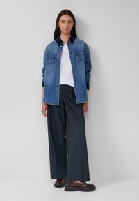 Veste en denim avec deux poches poitrine, couleur bleu clair, design à boutons. Assortie avec un pantalon large à rayures noires et des chaussures marron.
