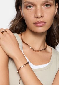 Smykkesæt i rosaguld inkluderer en kædestens halskæde, tyndt armbånd og ring med et rektangulært linkdesign og polerede detaljer.