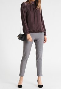 Luftig mørk lilla bluse med samlet halsudskæring, parret med skræddersyede grå bukser. En sort håndtaske og sorte spidse hæle fuldender outfittet.