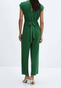 Mono verde con mangas de capucha, textura acanalada y un cinturón atado en la cintura. Presenta un diseño de espalda con abertura y una silueta de pierna ancha.