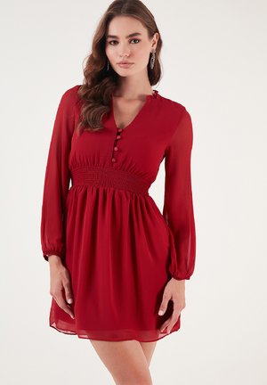 Red dress featuring a v-neck, long sheer sleeves, a smocked waist, and decorative buttons down the front, designed in lightweight fabric.