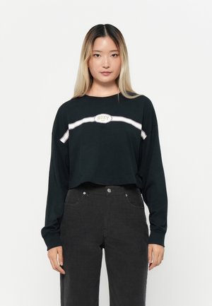 Zwarte longsleeve t-shirt met een witte horizontale streep en een ronde "ROXY" logo. Gecombineerd met donkergrijze hoge taillebroek.