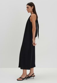 Abito maxi senza maniche di colore nero, con una silhouette rilassata, caratterizzato da un dettaglio di battente sul retro e spacchi laterali, realizzato in tessuto leggero.
