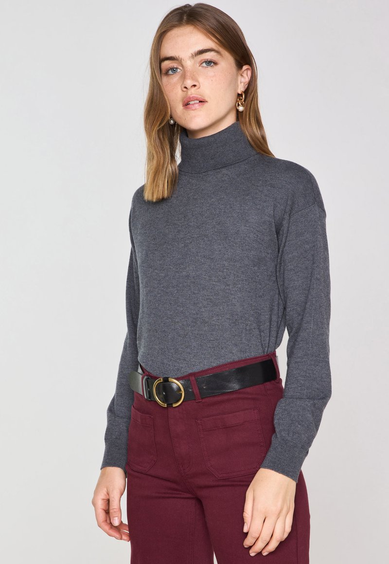 Maglione grigio a collo alto realizzato in morbido tessuto a maglia, abbinato a pantaloni bordeaux a vita alta e una cintura nera con una fibbia circolare dorata.