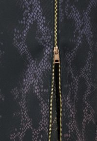 Primo piano di tessuto stampa serpente nero e viola con una cerniera dorata parzialmente aperta al centro.