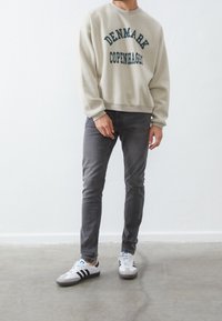 Krémová mikina s potiskem "DÁNSKO KODAŇ", spárovaná se šedými slim-fit džíny a bílými teniskami s černými pruhy a šedými akcenty.