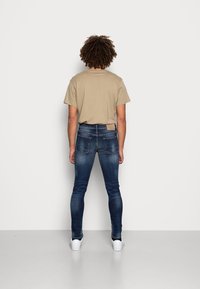 Beige t-shirt kombinerad med mörkblå denimjeans. Jeansen har en bakpatchetikett och två bakfickor, avslutat med vita sneakers.