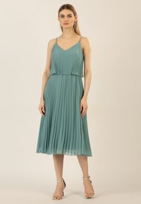 Faltenrockkleid in Teal mit verstellbaren Trägern, einem V-Ausschnitt und einer A-Linie, das aus einem fließenden Stoff mit einem Glanz am Saum besteht.