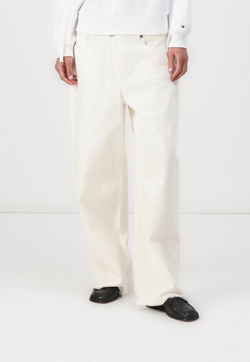 Pantaloni in denim bianchi a gamba larga con orlo sfrangiato, caratterizzati da una vestibilità rilassata e dal classico stile a cinque tasche. Indossati con scarpe nere.