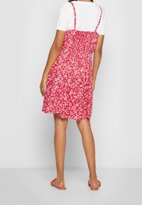 Röd blommig klänning med tunna band och smockad rygg, tillverkad av ett lätt och texturerat tyg med en utsvängd nederdel. Matchas med platta sandaler.