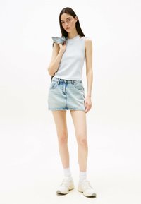 Lichtgrijze mouwloze top met uitsnede bij de schouders, gecombineerd met een lichtblauwe denim mini-rok. Model draagt witte sneakers en sokken.