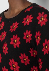 Schwarzer Pullover mit Rundhalsausschnitt, versehen mit einem floralen Muster aus roten Blumen mit gelben Zentren, strukturiertem Stoff und geripptem Kragen.