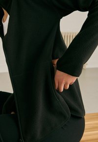 Giacca in pile nera con finitura testurizzata, zip frontale e tasche laterali. Progettata con maniche lunghe e vestibilità rilassata.