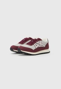 Chaussures de sport avec une tige en maille grise et des accents en daim bordeaux, détail de logo blanc et semelle en caoutchouc noir texturé.