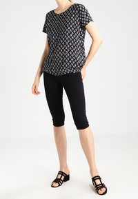 Top de manga corta con patrón en blanco y negro combinado con leggings capri negros y sandalias negras con tiras, que presenta un ajuste holgado y una textura suave.
