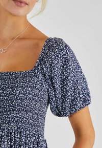 Rochie bleumarin cu imprimeu floral, cu decolteu pătrat, mâneci bufante și bust elastic, având mici modele de flori albe pe întreaga suprafață.