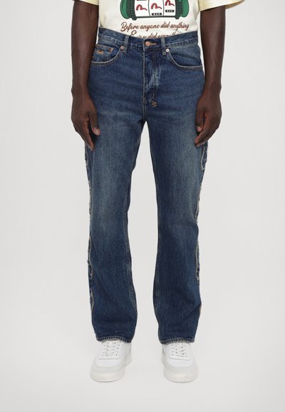 Blå denim jeans med en løs pasform, featuring huller langs de ydre sømme, færdiggjort med kobber hardware og et klassisk fem-lomme design.