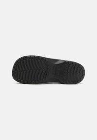 Semelle de chaussure en caoutchouc noir avec une surface texturée. Présente un motif en chevrons et des accents de grip circulaires pour une meilleure traction.