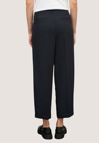 Donkerblauwe, wijde broekspijpen van een gladde stof, met twee achterzakken en opgerolde broekspijpen, gecombineerd met zwarte schoenen.