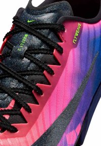 Gros plan sur une chaussure de course Nike multicolore avec des lacets noirs, une languette noire scintillante, des côtés roses et violets, et un texte vert néon indiquant "MAXFLY 2" et "FLYWEAVE".