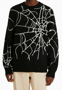 Svart tröja med vitt spindelnätsmönster, rund hals, långa ärmar och mjuk textur. Har kontrastsömmar och avslappnad passform.