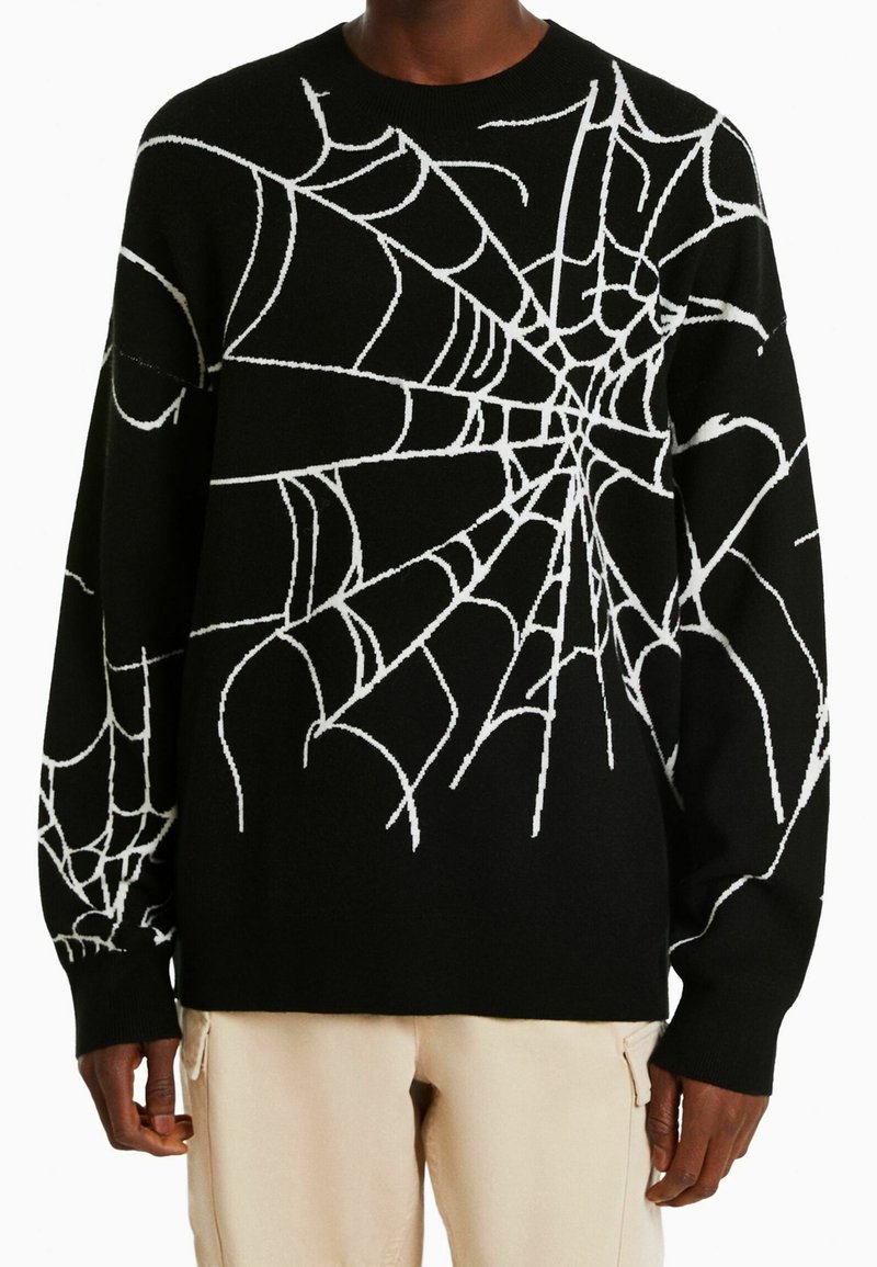 Svart tröja med vitt spindelnätsmönster, rund hals, långa ärmar och mjuk textur. Har kontrastsömmar och avslappnad passform.