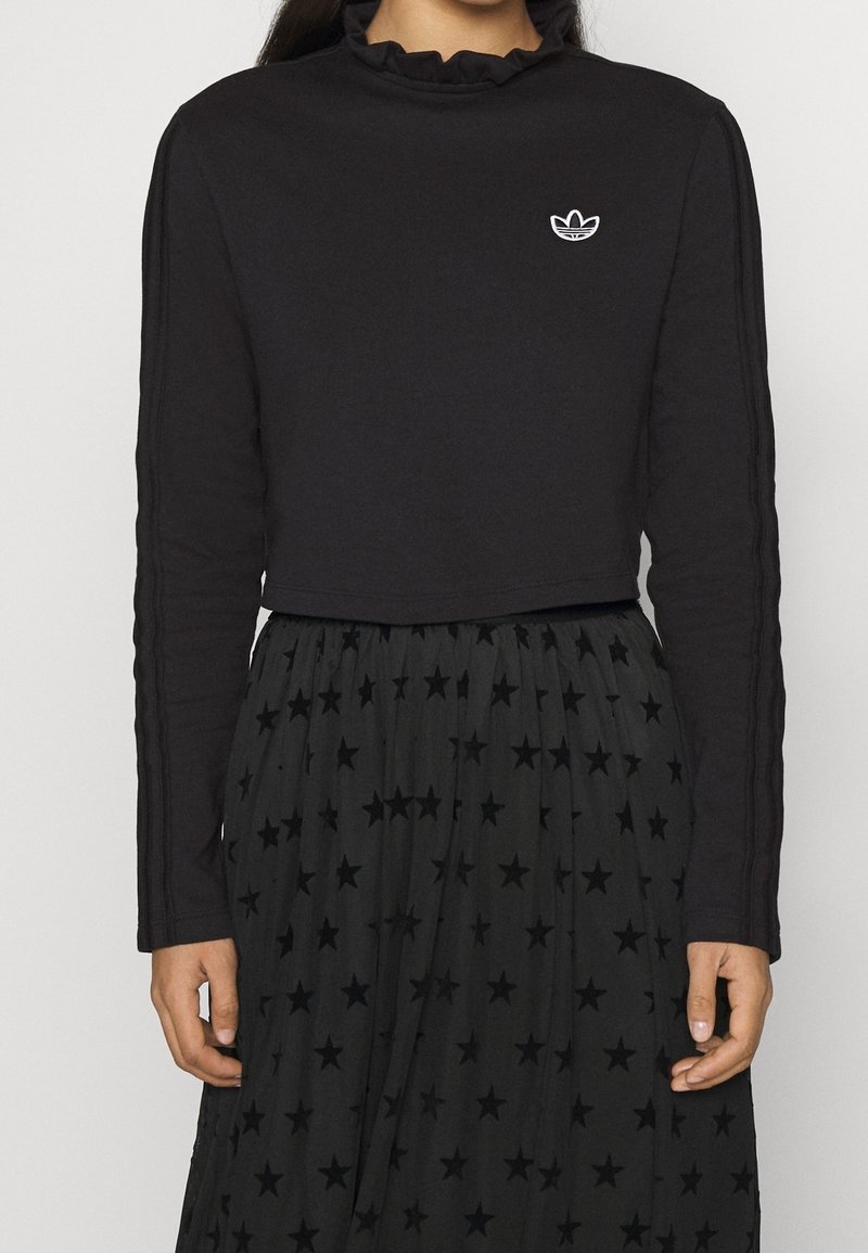 Svart kortärmad topp med rynkad halslinning och broderad vit logotyp. Matchas med en svart kjol med stjärnmönster.