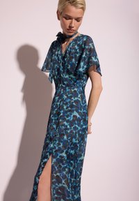 Sukienka w kwiatowy wzór w niebiesko-zielonym szyfonie, z krótkimi rękawami, wiązaniem przy szyi oraz rozcięciem sięgającym ud. Gładka faktura, luźny krój.