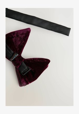 Burgundy velvet bow tie with a black adjustable strap and side clasp, featuring a soft texture and pointed ends.