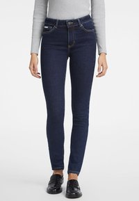 Jeans pitillo de talle alto en azul oscuro con una textura de denim suave, presillas para cinturón, bolsillos delanteros y traseros, y sutiles detalles de costura.