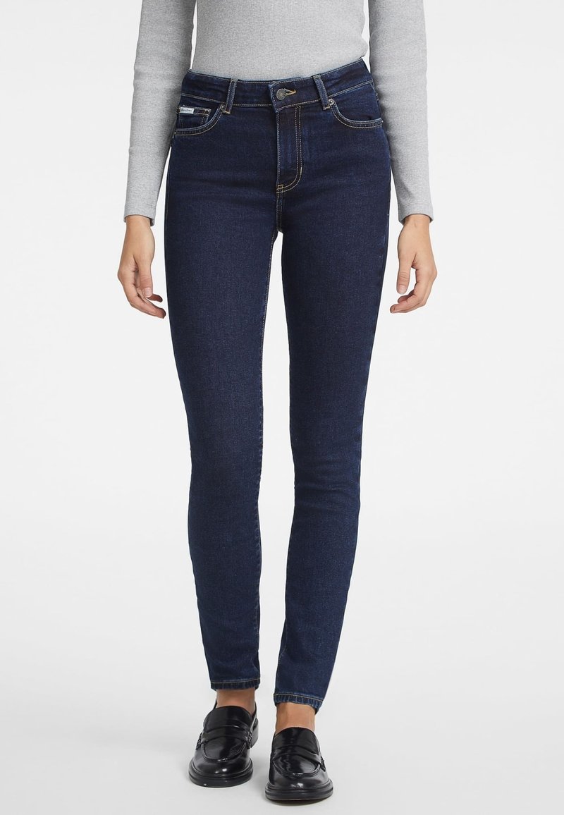 Jeans pitillo de talle alto en azul oscuro con una textura de denim suave, presillas para cinturón, bolsillos delanteros y traseros, y sutiles detalles de costura.