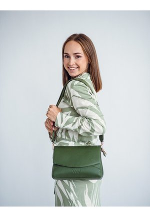 Green faux leather handbag with a flap closure, featuring a subtle embossed logo, adjustable strap, and a smooth texture, held by a model.