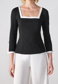 Haut noir ajusté avec un décolleté carré, des manches trois-quarts, et un bord blanc sur les manches et le col. Texture de tissu lisse.