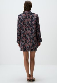 Blazer à motifs en marine foncé, avec un design floral rouge et crème. Manches longues, détail de col et texture lisse.