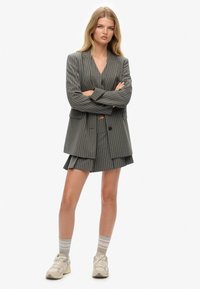 Blazer a rayas grises con falda mini plegada a juego. Llevado sobre una camiseta negra, combinado con medias a rayas grises y zapatillas crema.