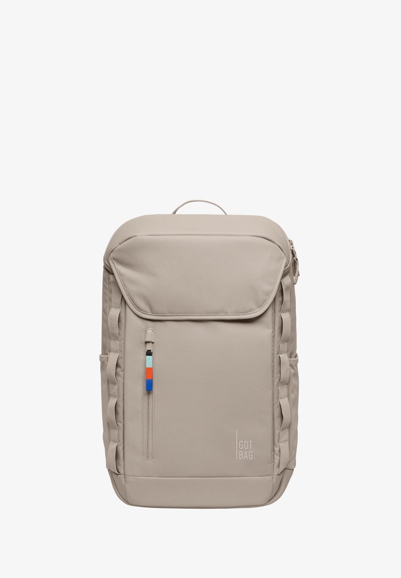 Mochila beige con una parte superior redondeada, que cuenta con un bolsillo frontal con cremallera y un tirador de cremallera multicolor, correas laterales y un logo en la parte inferior.