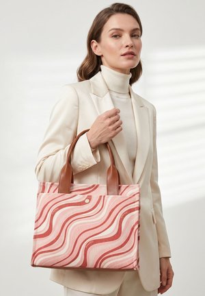 Vrouw in wit pak houdt een roze en rode tas met golvend patroon en bruine handvatten vast tegen een lichte achtergrond.