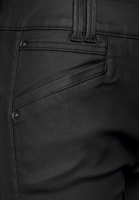 Svarta syntetbyxor med en slät yta, med en diagonal fickdesign och kontrasterande sömnadsdetaljer.