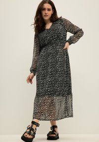 Vestido negro de manga larga con un estampado de leopardo floral translúcido, cintura fruncida y dobladillo fluido. Combinado con sandalias negras de tiras.
