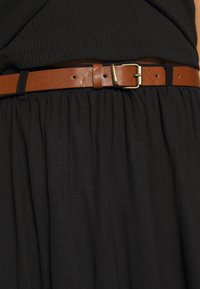 Cinturón de cuero marrón con hebilla dorada, usado sobre una prenda de tela negra con textura fruncida, que muestra un diseño simple y limpio.