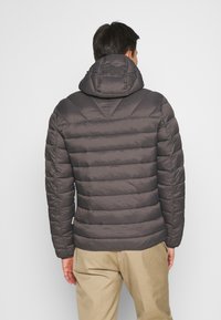 Pufferjakke i mørkegrå med quiltet design, fastgjort hætte og ribbede manchetter. Har en lige nederkant og minimal branding.