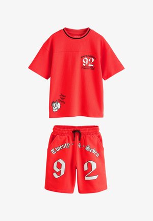 Rødt sæt med kortærmet skjorte og shorts med teksten "92" og "Twenty-4-Seven", kranietryk og sort snøre i elastikliv på shortsene.