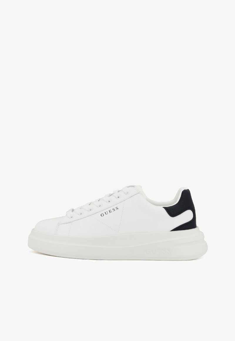 Baskets blanches avec une tige lisse en simili cuir, dotées d'un accent noir au niveau du talon et d'une semelle blanche épaisse et texturée. Logo "GUESS" visible.