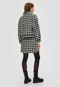 Mustvalge houndstooth-stiilis jope ja seeliku komplekt tekstuuriga kangast. Mudel kannab musti sukkpükse ja pahkluu saapaid ning lõige on lühike jope.