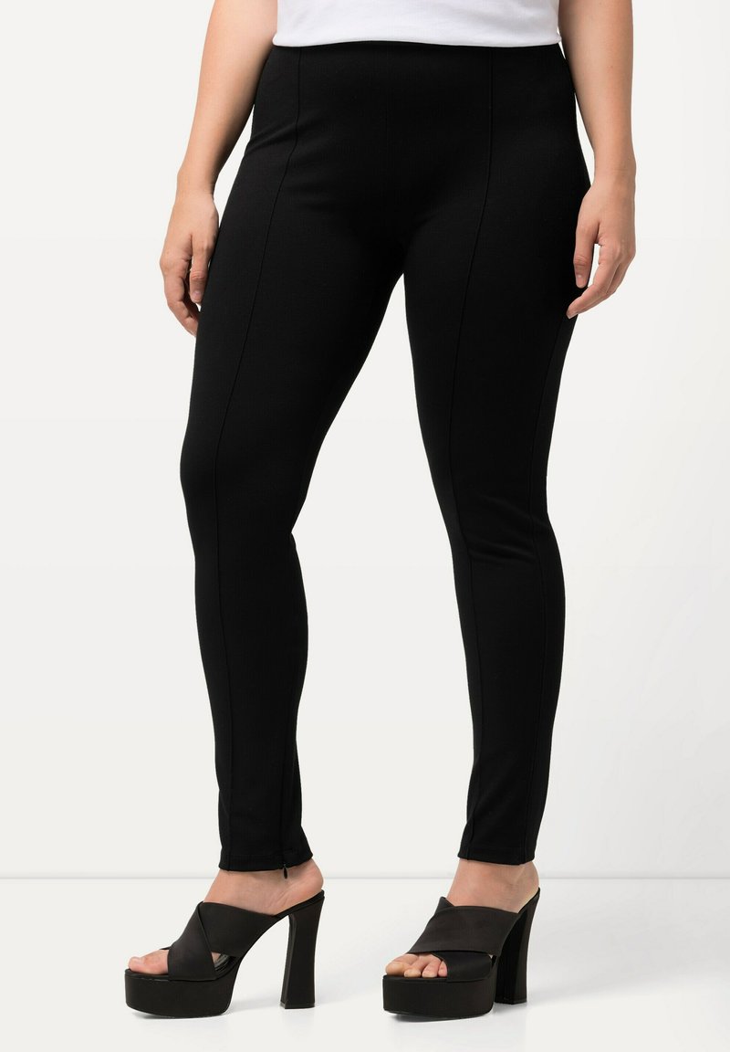 Zwarte leggings van een gladde, rekbare stof met contrasterende stiksels. Draag ze met zwarte platform sandalen, wat het stijlvolle ontwerp benadrukt.
