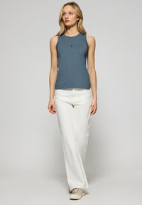 Bezramieniowy, dopasowany, niebieski bawełniany top na ramiączkach z okrągłym dekoltem i małym logo. Połączony z białymi, szerokimi spodniami i beżowymi trampkami.