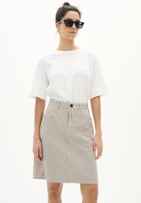 T-shirt blanc à manches courtes associé à une jupe rayée beige et noire avec une fermeture à boutons et une silhouette légèrement évasée.