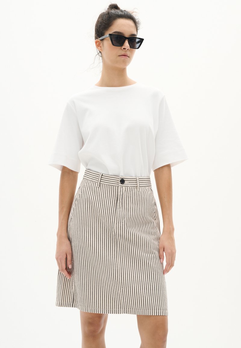 T-shirt blanc à manches courtes associé à une jupe rayée beige et noire avec une fermeture à boutons et une silhouette légèrement évasée.