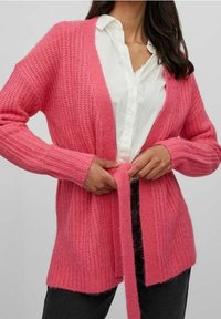 Jasně růžový pletený kardigan s výstřihem do V, otevřeným předním dílem a dlouhými rukávy. Má pás na zavázání v pase a žebrované lemy na rukávech.